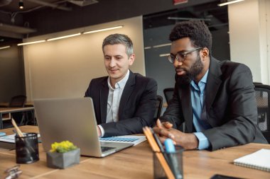 İşlem devam ediyor. İki işadamı dizüstü bilgisayarın başında oturuyor ve proje üzerinde çalışıyorlar.
