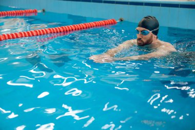 Sürünerek yüzme stili. Siyah yüzme şapkalı adam havuzda sürünerek yüzüyor.