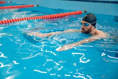 Sürünerek yüzme stili. Siyah yüzme şapkalı adam havuzda sürünerek yüzüyor.