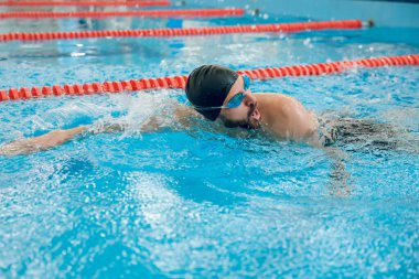 Sürünerek yüzme stili. Siyah yüzme şapkalı adam havuzda sürünerek yüzüyor.