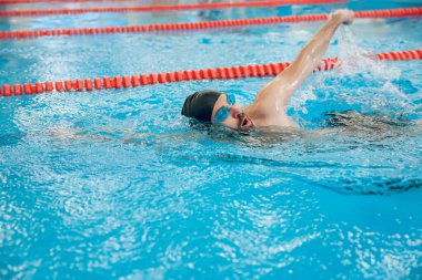Sürünerek yüzme stili. Siyah yüzme şapkalı adam havuzda sürünerek yüzüyor.