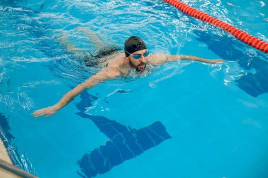 Sürünerek yüzme stili. Siyah yüzme şapkalı adam havuzda sürünerek yüzüyor.
