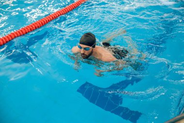 Sürünerek yüzme stili. Siyah yüzme şapkalı adam havuzda sürünerek yüzüyor.