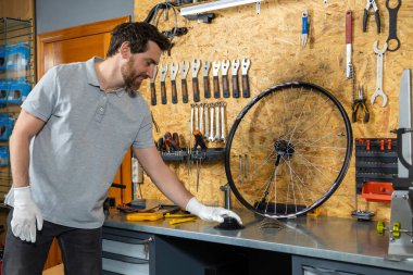 Beyaz eldivenli tamirci atölyede aletlerle bisiklet tekerleği tutuyor.