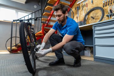 Tamirci atölyede eldivenli ellerle bisiklet tekerleğini tamir ediyor.