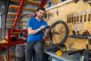 Mavi gömlekli tamirci atölyedeki araçların yanında cep telefonu kullanıyor.