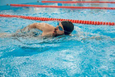 Sürünerek yüzme stili. Siyah yüzme şapkalı adam havuzda sürünerek yüzüyor.