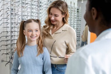 Optik dükkan. Anne ve kızı optik dükkanında yeni gözlük seçiyorlar ve ilgileniyorlar.