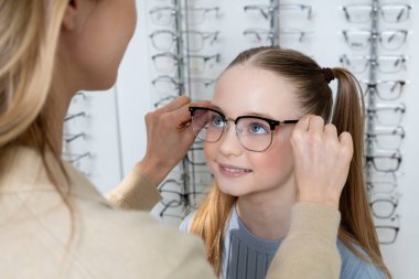 Optik dükkanında. Anne ve kızı optik dükkanında yeni gözlük seçtikten sonra pozitif görünüyor.