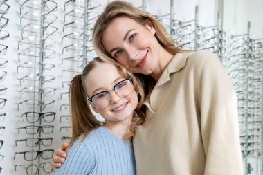 Optik dükkanında. Anne ve kızı optik dükkanında yeni gözlük seçtikten sonra pozitif görünüyor.