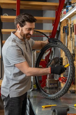 Siyah eldivenli tamirci atölyede aletlerle bisiklet çarkını inceliyor.