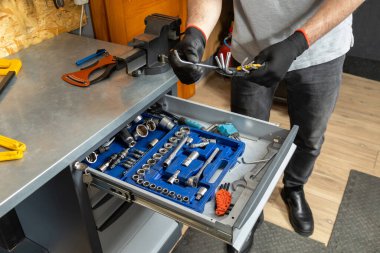 Siyah eldivenli tanınmayan bir tamirci atölyedeki bisiklet parçaları yanında alet kullanıyor.