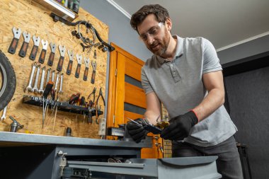 Siyah eldivenli tamirci bisiklet parçaları ile atölyede araçları denetliyor