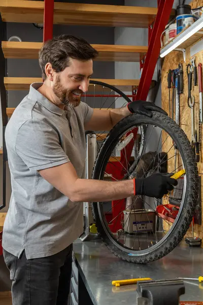 Siyah eldivenli tamirci atölyede aletlerle bisiklet çarkını inceliyor.