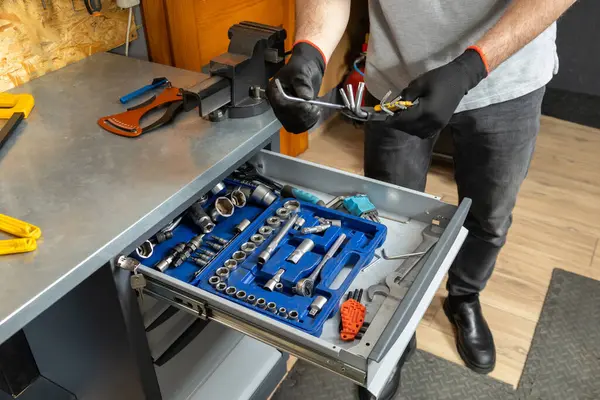 Siyah eldivenli tanınmayan bir tamirci atölyedeki bisiklet parçaları yanında alet kullanıyor.