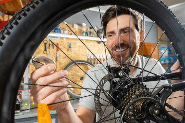 Beyaz eldivenli tamirci atölyede aletlerle bisiklet tekerleği tutuyor.