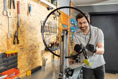 Siyah eldivenli tamirci atölyede bisiklet tekerleğini ayarlıyor.