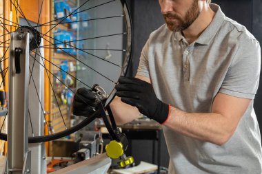 Atölye ortamında siyah eldivenli tamirci bisiklet tekerleğini inceliyor.