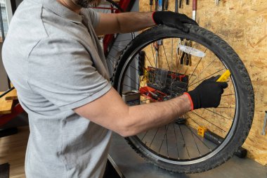 Siyah eldivenli tamirci atölye ortamında bisiklet tekerleğini ayarlıyor