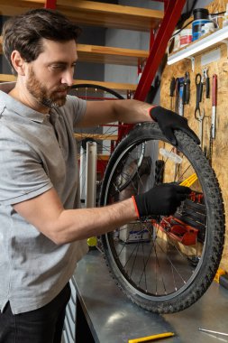 Siyah eldivenli tamirci atölyede aletlerle bisiklet tekerleğini kaldırıyor.