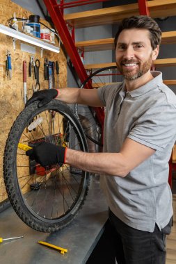 Siyah eldivenli tamirci atölyede aletlerle bisiklet tekerleği tutuyor.