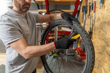 Siyah eldivenli tamirci atölyede aletlerle bisiklet tekeri üzerinde çalışıyor.