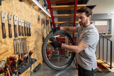 Siyah eldivenli tamirci atölyede aletlerle bisiklet tekerleği tutuyor.