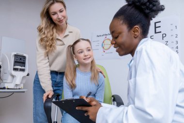 Vizyon testi. Sarışın bir kız ve annesi göz doktorunda danışmanlık yapıyorlar.