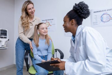 Vizyon testi. Sarışın bir kız ve annesi göz doktorunda danışmanlık yapıyorlar.