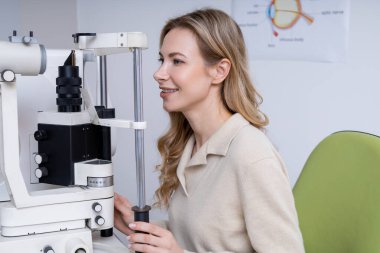 Vizyon testi. Sarışın, genç, beyaz bir kadın optik ekipman üzerinde görüş testi yapıyor.