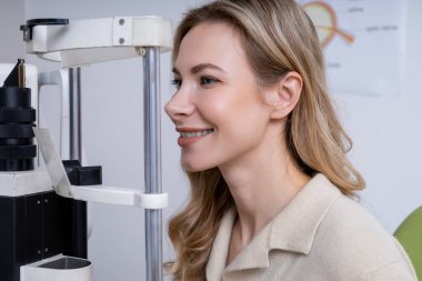 Vizyon testi. Sarışın, genç, beyaz bir kadın optik ekipman üzerinde görüş testi yapıyor.