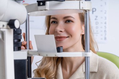 Vizyon testi. Sarışın, genç, beyaz bir kadın optik ekipman üzerinde görüş testi yapıyor.