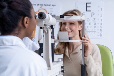 Vizyon testi. Sarışın, genç, beyaz bir kadın optik ekipman üzerinde görüş testi yapıyor.