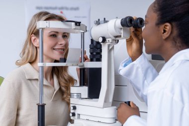 Vizyon testi. Sarışın, genç, beyaz bir kadın optik ekipman üzerinde görüş testi yapıyor.