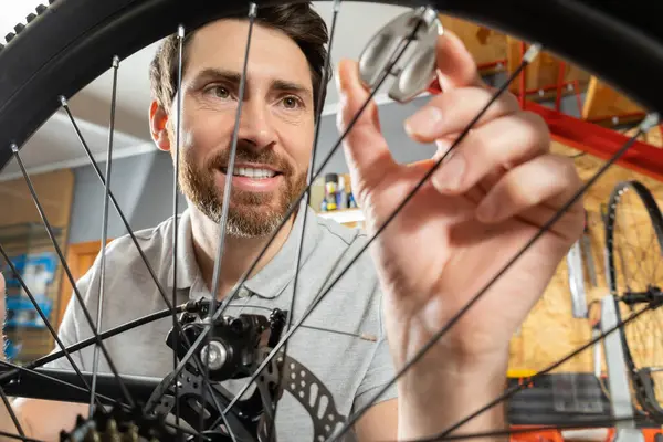 Tamirci atölye ortamında ellerle bisiklet tekerleğini inceliyor.