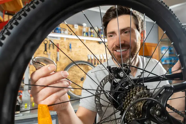 Beyaz eldivenli tamirci atölyede aletlerle bisiklet tekerleği tutuyor.