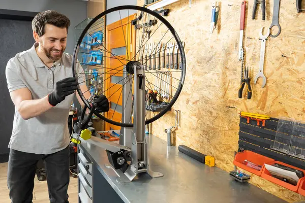 Siyah eldivenli tamirci atölyede aletlerle bisiklet tekerleği tutuyor.