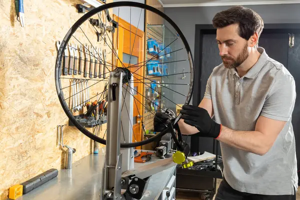Siyah eldivenli tamirci atölyede bisiklet tekerleğini ayarlıyor.