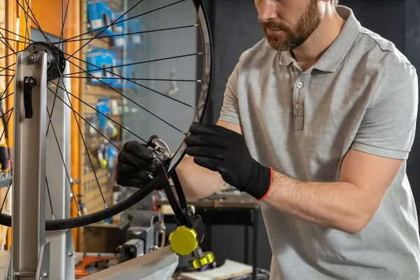 Atölye ortamında siyah eldivenli tamirci bisiklet tekerleğini inceliyor.