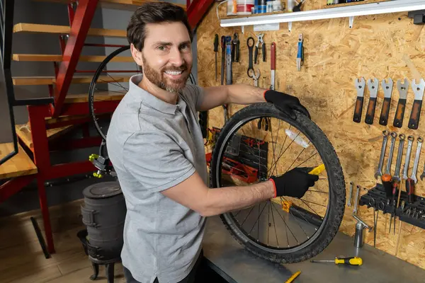 Siyah eldivenli tamirci atölyede bisiklet çarkını inceliyor.