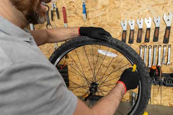 Atölyede siyah eldivenli tamirci bisiklet tekerini kaldırıyor.
