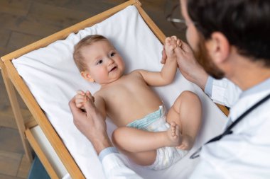 Doktorlarda. Doktor ofisinde küçük bir çocuğu muayene ediyor ve konsantre görünüyor.