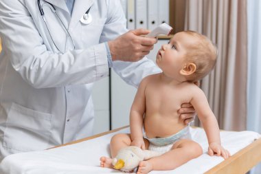 Sıcaklık kontrolü. Muayene sırasında küçük bir çocuğun sıcaklığını ölçen çocuk doktoru.