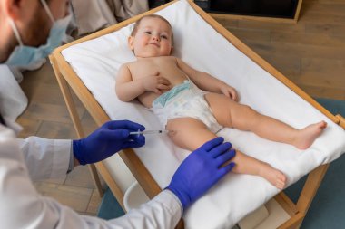 Aşılama. Doktor ona aşı yaparken tatlı bir erkek bebek masada yatıyor.