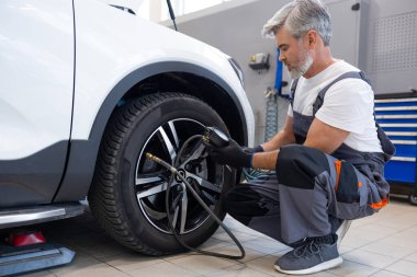 Araç gereçlerin arasında basınç göstergesi kullanarak araba lastiğini şişirme atölyesindeki tamirci