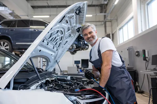 Oto tamir atölyesinde kaputu açık aracın yanında çalışan tamirci.