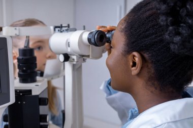 Optik ekipman. Hasta ile çalışırken optik tıbbi araç kullanan kadın göz doktoru