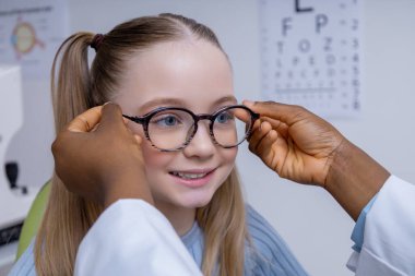Optometristin ofisinde. Göz doktorunun ofisinde yeni gözlük deneyen beyaz tatlı bir kız.
