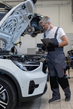 Oto tamir atölyesinde kaputu açık motor kontrolü için tablet kullanan tamirci