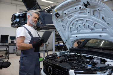 Tamirci otomobil tamirhanesinde motor kaputu açık tabletle teşhis koyuyor.